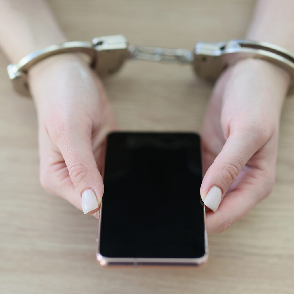 A person in cuffs with a cell phone