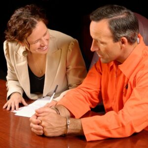 Lawyer consulting with handcuffed prisoner in an orange jumpsuit.